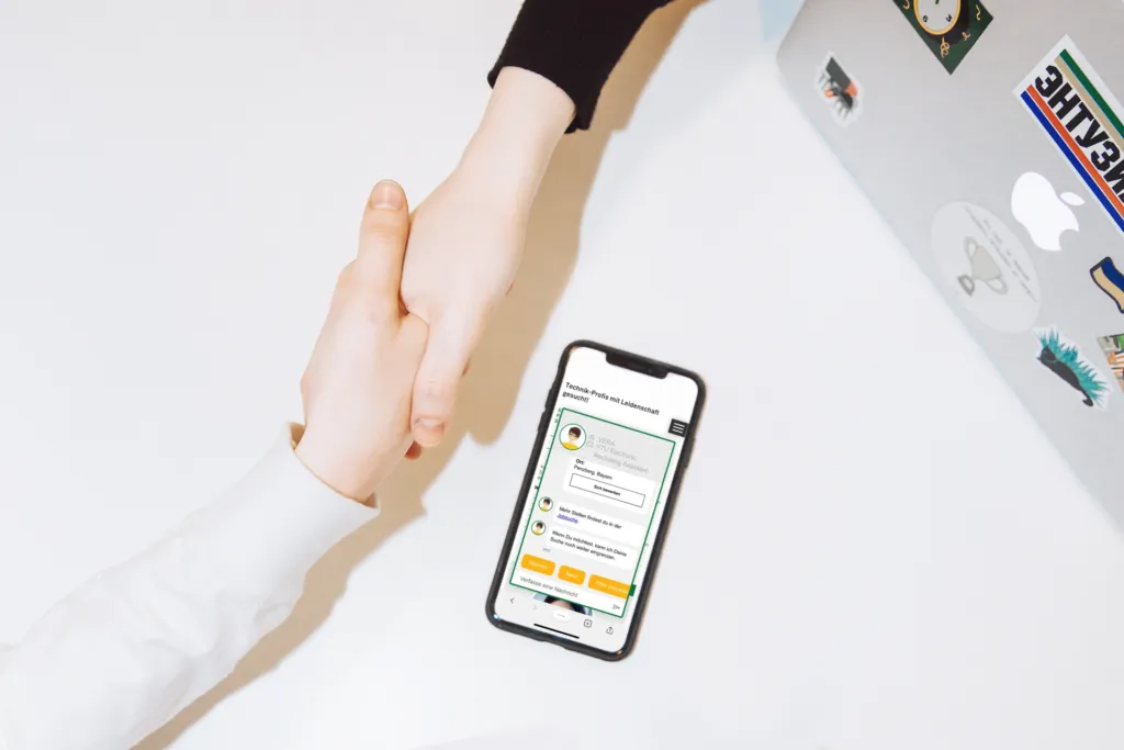 Smartphone mit Recruiting-Chatbot neben einem Handschlag